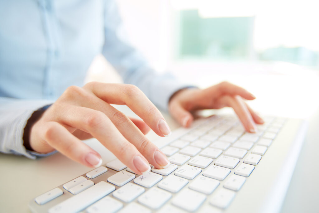 Close-up of a person typing on a white computer keyboard in a bright office environment